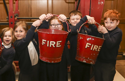 Lots of children holding up old fire buckets