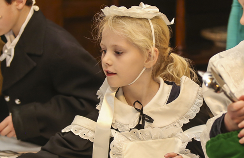 A little girl dressed in Victorian maids costume setting a table with crystal ware