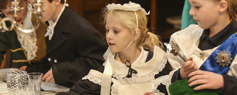 A little girl dressed in Victorian maids costume setting a table with crystal ware