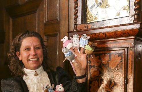 a woman in a victorian costume standing next to a grandfather clock with mouse finger puppets