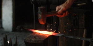 hand holding a hammer beating a glowing piece of iron