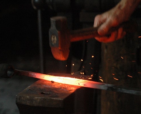 hand holding a hammer beating a glowing piece of iron