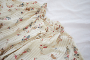 Close up of the collar of a cream coloured striped dress with a pattern of blue and red flowers