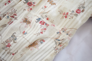 Close up of cream coloured, striped cotton fabric with a pattern of blue and red flowers and brown leaves
