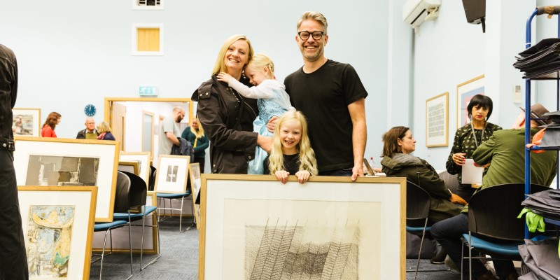 Two parents and two children smiling and holding a framed picture from the picture library
