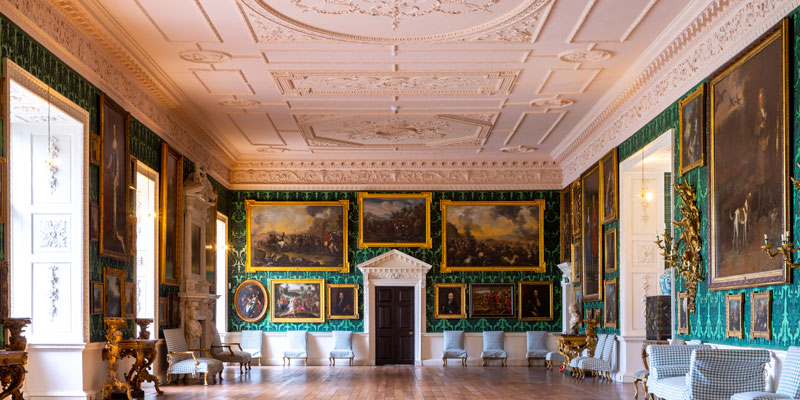 The grand hall at Temple Newsam House featuring paintings and decorative furniture, with ornate turquoise wallpaper, highly decorated ceiling, and wooden floors.
