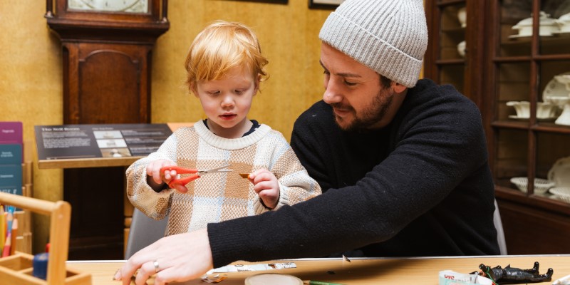 a man and young child holding scissors and doing craft activities together