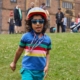 running child wearing sunglasses, cycling helmet and gold medal with temple newsam house in the background