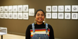 A young woman smiling at the camera in front of a gallery wall