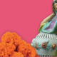 A statue of a woman with an urn set against a pink background and a bottom border of orange marigolds.