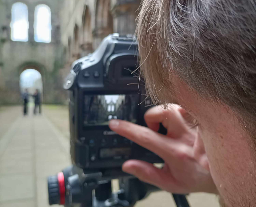 The side of a mans face looking through a camera at Kirkstall Abbey