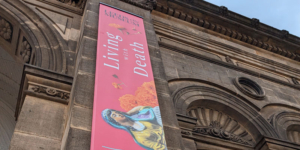 A section of the exterior of Leeds City Museum building with a large vertical banner to advertise the exhibition - Living with Death.