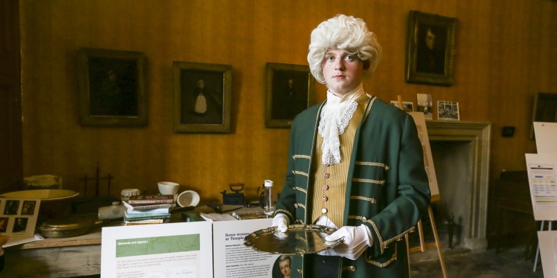 a young person dressed as an 18th century servant wearing a wig and carrying a tray
