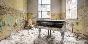 An abandoned grand piano in a room with peeling wallpaper