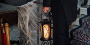 A hand holding a lantern and a chain, in front of a staircase with cobwebs on