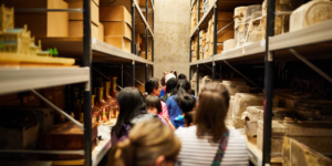 A group of people looking down a corridor of shelves with boxes and ancient ruins on